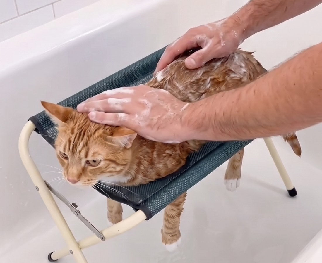 A cat lying flat on the Groom Cradle in a bathtub, legs through the mesh